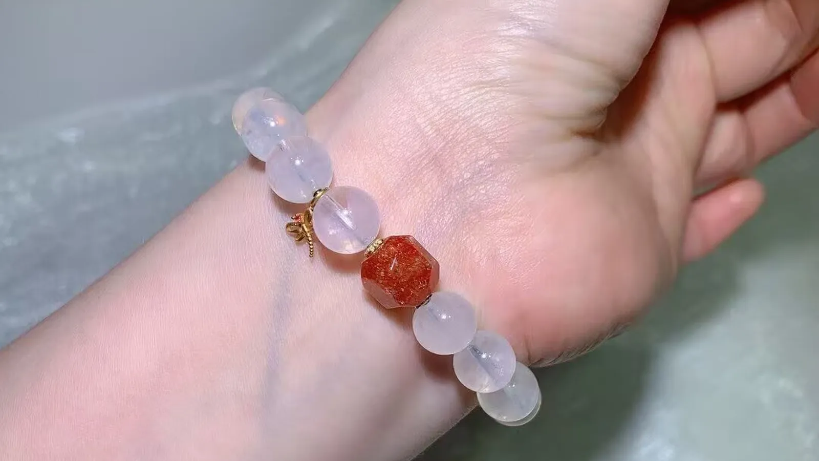 手腕上的蓝针水晶手链:冰透乳白色珠子,配一颗切面珊瑚橙色珠和小巧的古法饰品