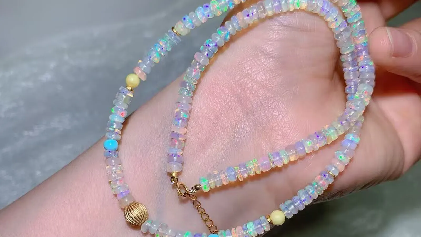 手中的 4.7mm 欧泊串珠项链:闪着彩虹变彩的白色欧泊片珠,配复古风棱纹圆珠和延长链